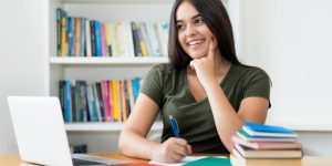 Laughing spanish female student learning at desk indoors at library